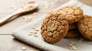 Biscotti all’avena dorati su un canovaccio, con fiocchi d’avena sparsi e un cucchiaio di legno sullo sfondo
