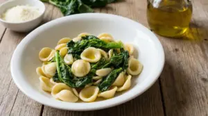 Orecchiette con cime di rapa in piatto bianco su tavolo in legno, con olio extravergine d'oliva a lato
