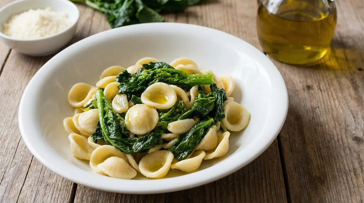 Orecchiette con cime di rapa in piatto bianco su tavolo in legno, con olio extravergine d'oliva a lato