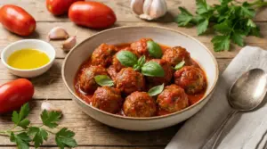 Polpette al sugo di pomodoro in ciotola, guarnite con basilico, con pomodori e aglio su tavolo di legno